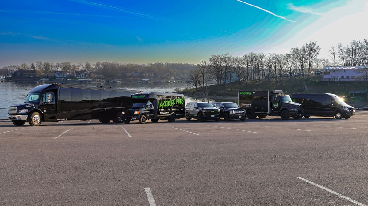 Lake Ride Pros luxury transportation fleet lined up at Lake of the Ozarks including limo bus, Rescue Squad truck, SUVs, and Mercedes Sprinter vans with lake view in background